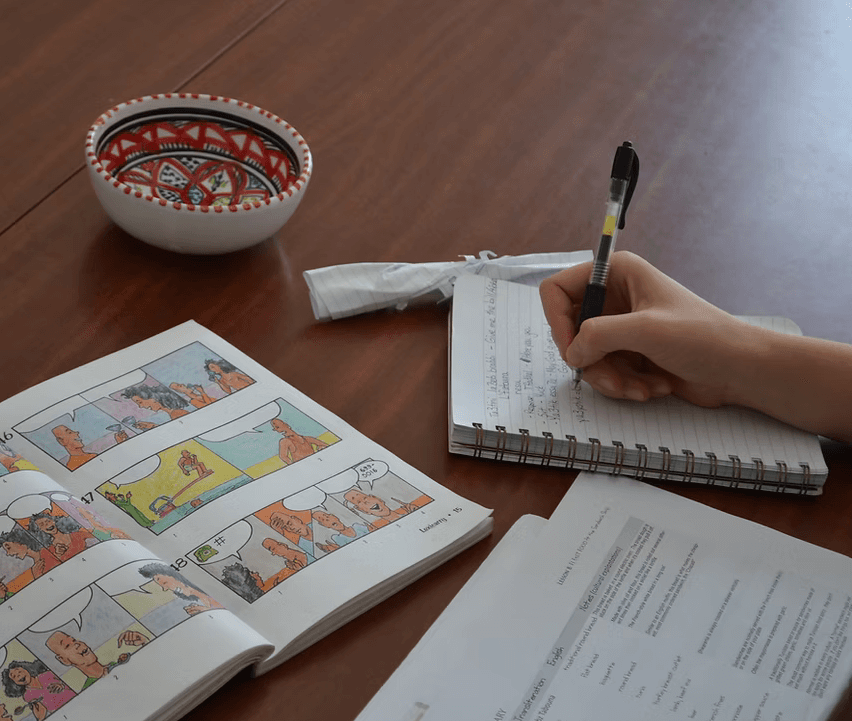 A student learning Tunisian Arabic with a workbook and notes